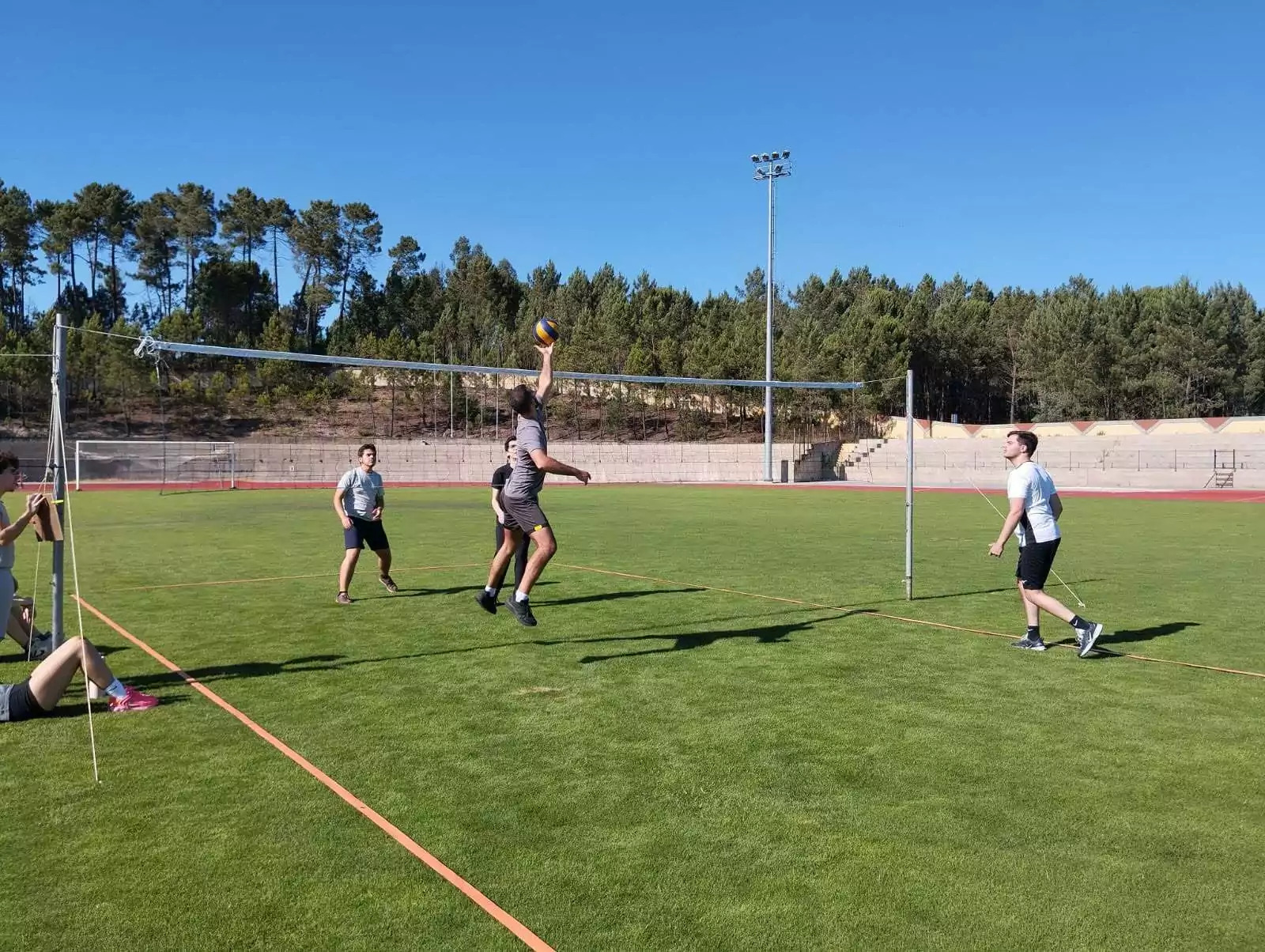 Jovens disputam uma partida de voleibol no campo de relva