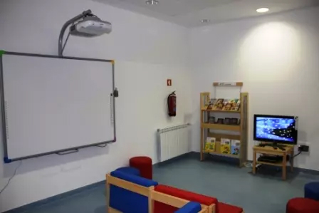 Sala educativa com quadro interativo, livros, televisão e cadeiras infantis