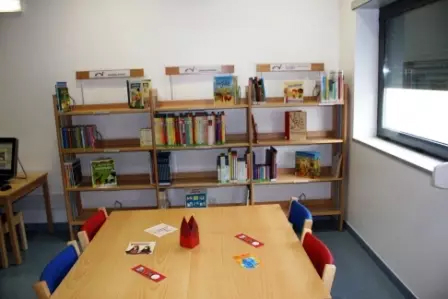 Sala de leitura com estantes, livros e mesa para crianças