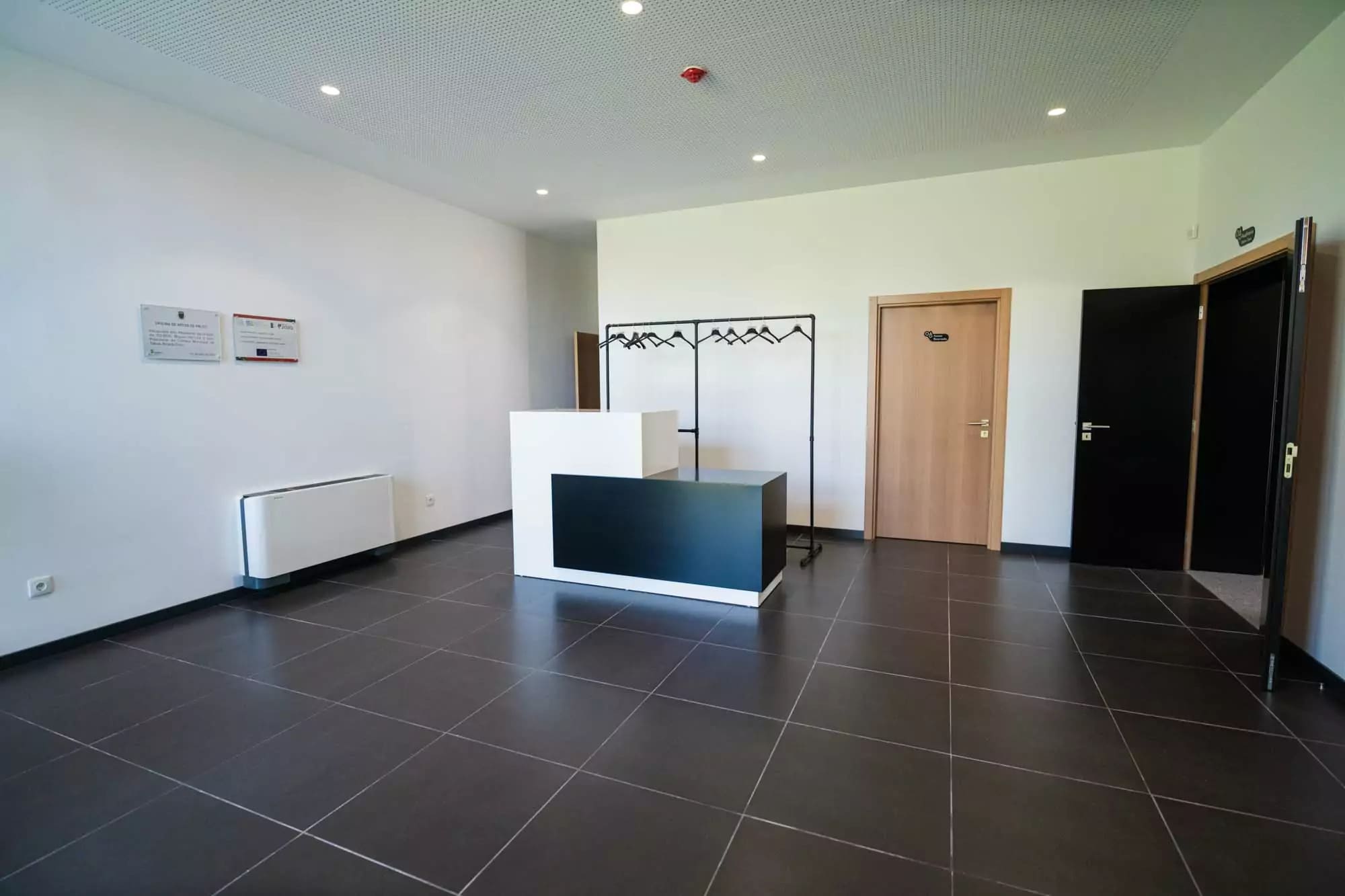 Área de receção e átrio da Oficina de Artes de Palco, com balcão preto e branco e charriot d...