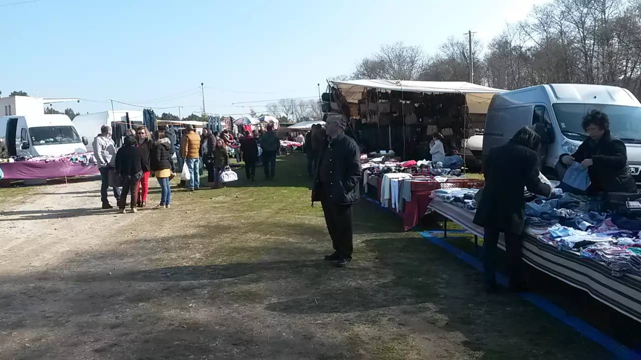 Visitantes percorrem uma feira ao ar livre com bancas de roupa