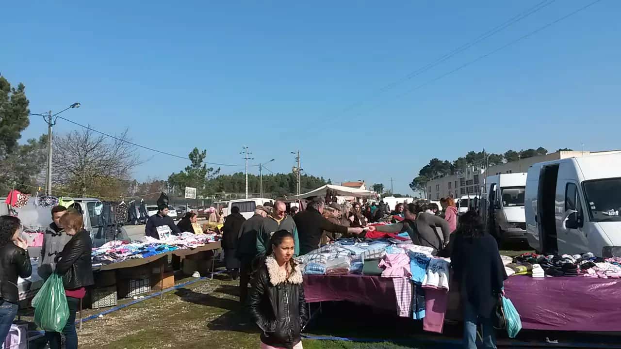 Bancas de roupa e visitantes numa feira ao ar livre