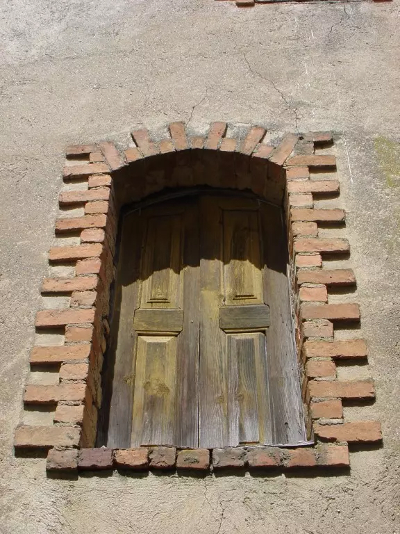 Porta de madeira com moldura de tijolo numa fachada em Candosa