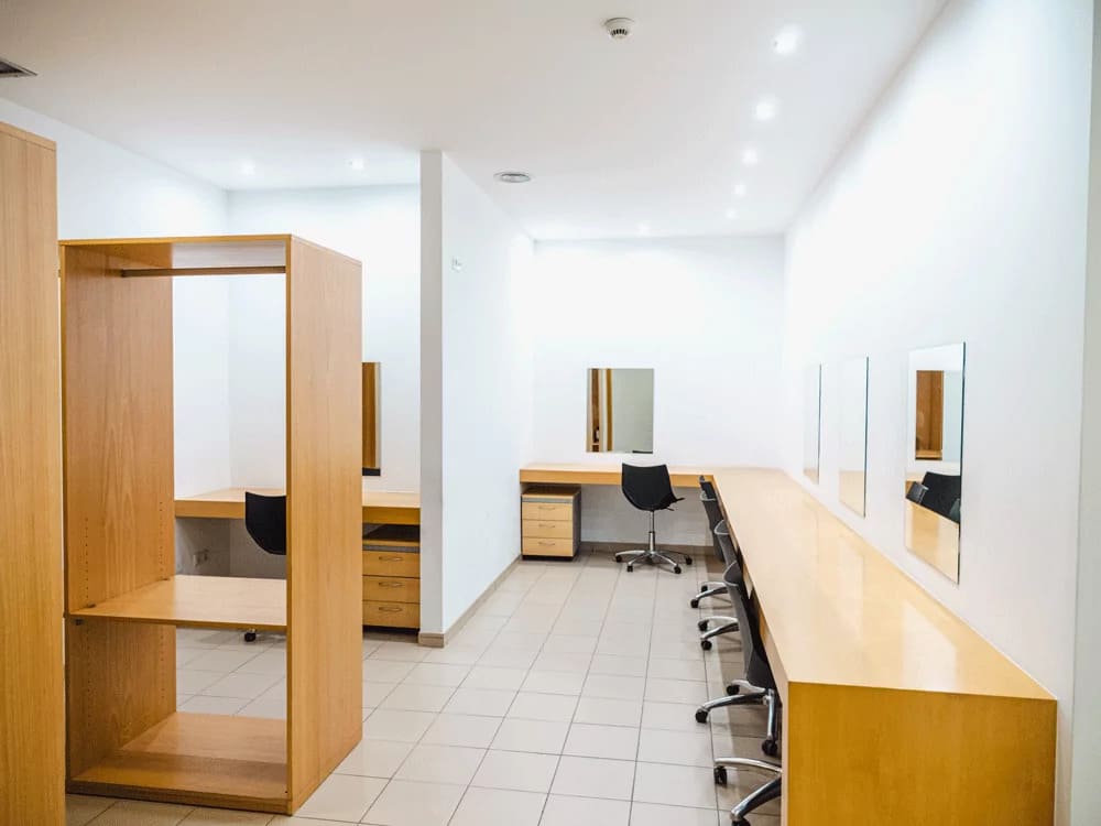Camarim do Centro Cultural com bancadas em madeira, espelhos de camarim e cadeiras de escritório.