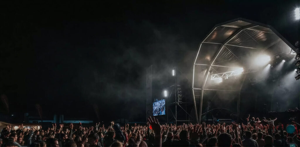 Público assiste a um espetáculo noturno com estrutura luminosa no palco