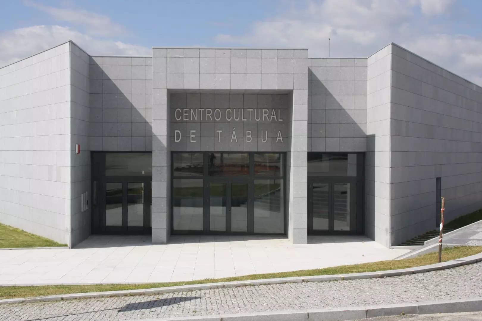 Fachada principal do edifício do Centro Cultural de Tábua em revestimento cinzento com portas d...