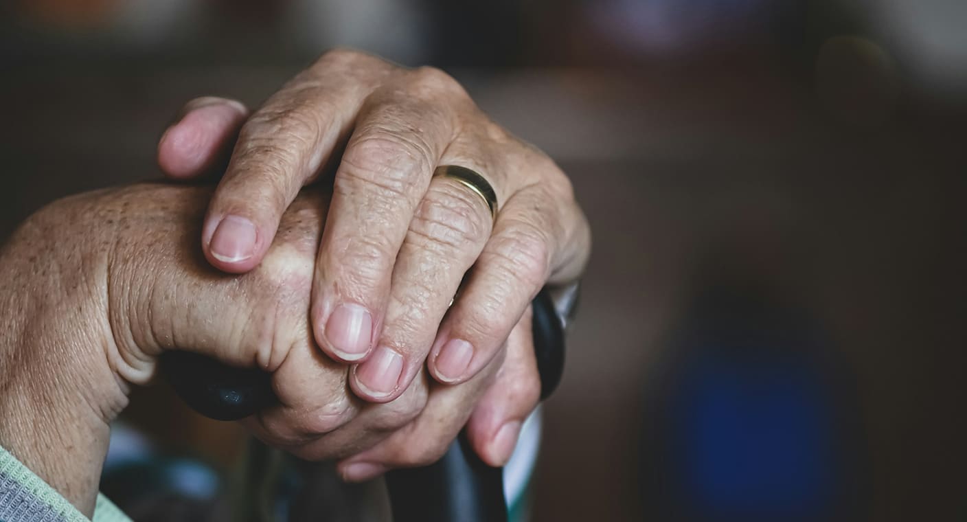 Duas mãos de uma pessoa idosa apoiadas numa bengala