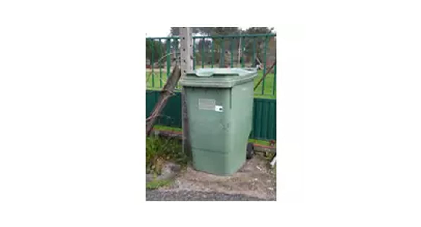 Contentor verde instalado junto a uma vedação