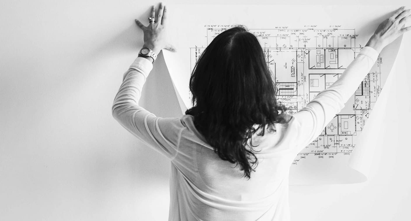 Pessoa analisa uma planta de arquitetura afixada na parede