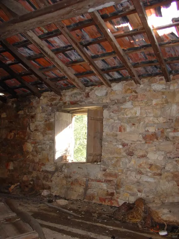 Interior de uma construção antiga com paredes de pedra e telhado degradado
